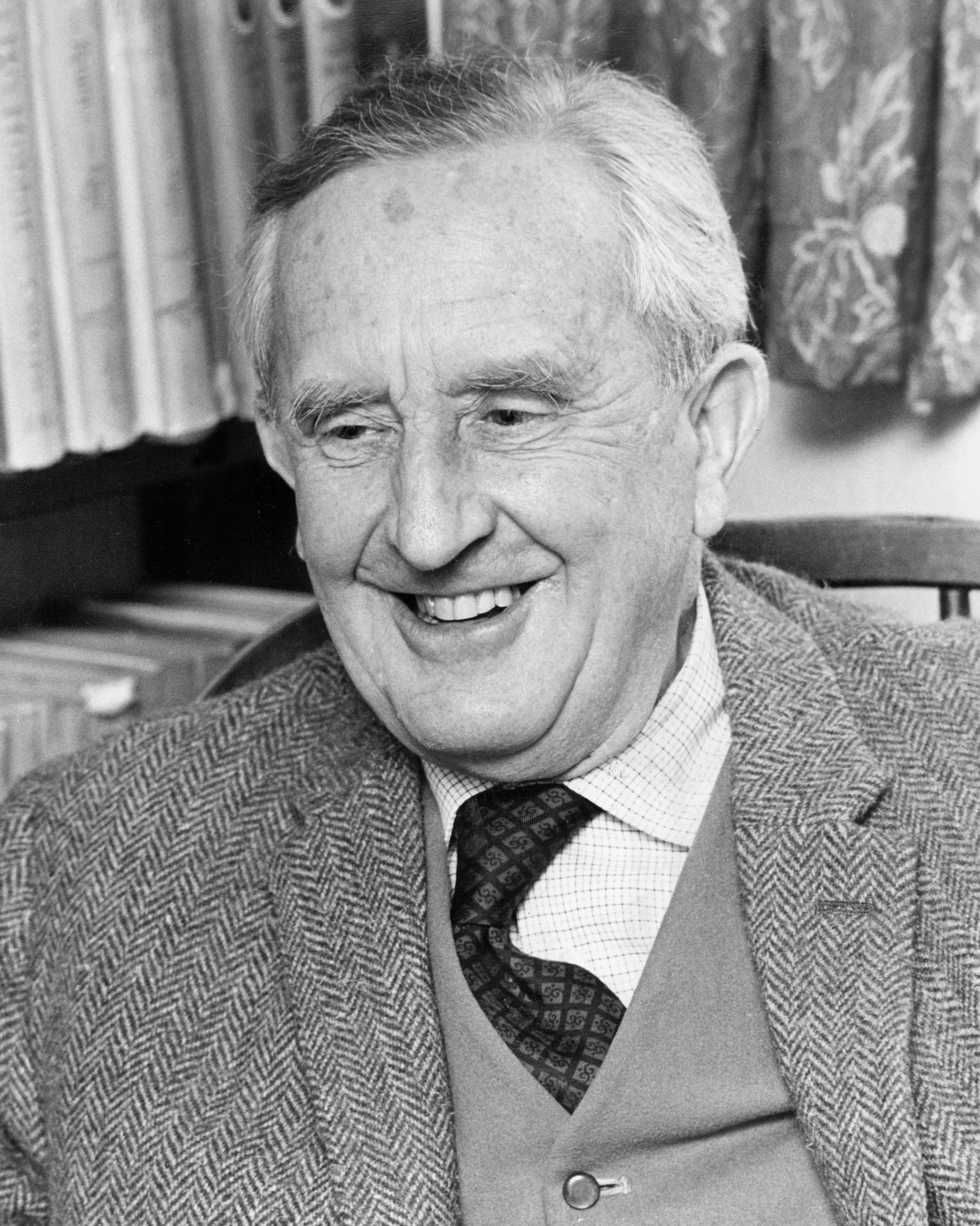 Photo : John Ronald Reuel Tolkien, riant près de sa bibliothèque, au 76 Sandfield Road à Oxford, année 1961.