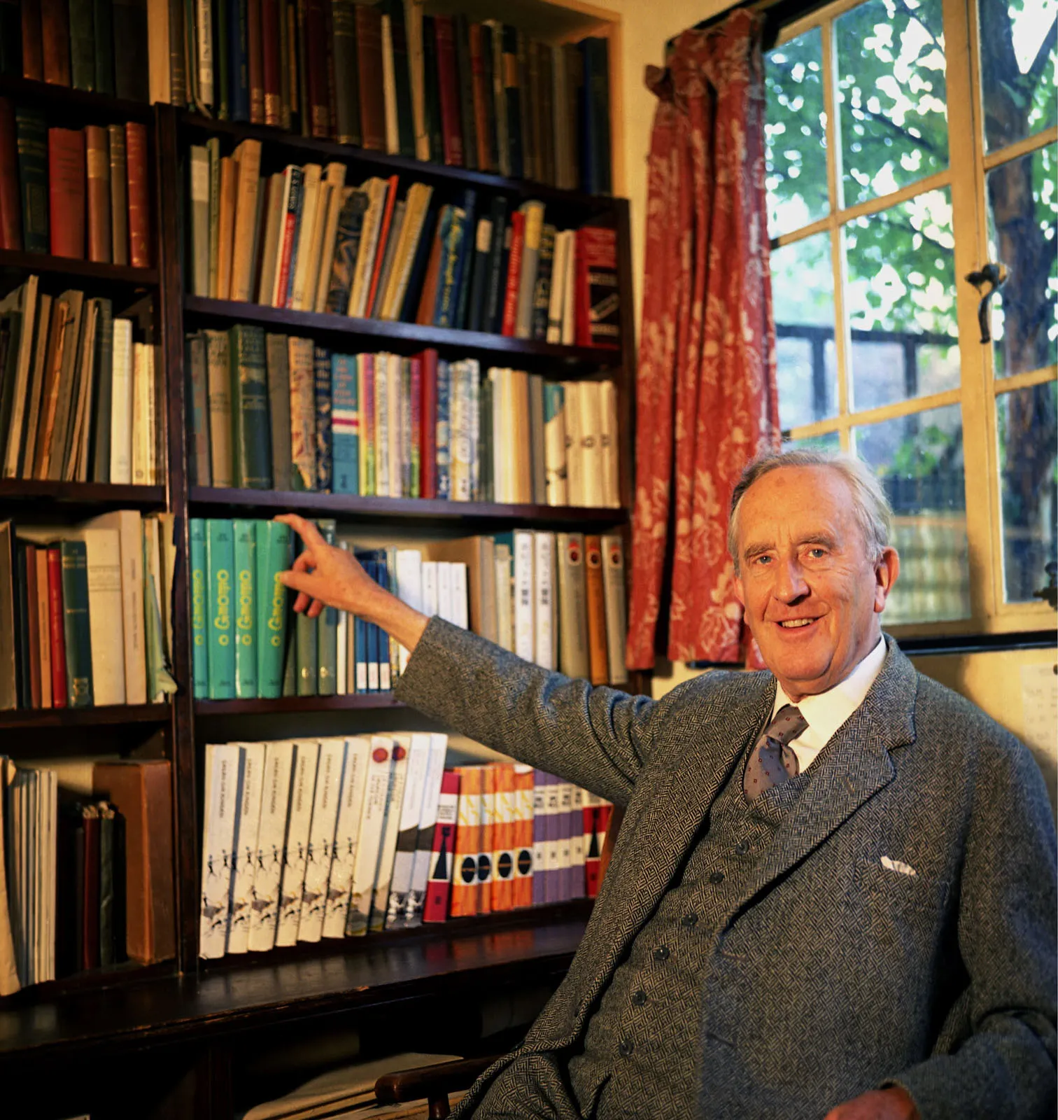 Photo : John Ronald Reuel Tolkien, tirant un livre de sa bibliothèque, au 76 Sandfield Road à Oxford, année 1961.